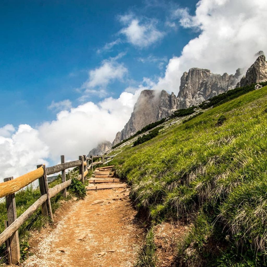 Un sentiero escursionistico tra prati verdi e cime alpine durante una giornata estiva in montagna