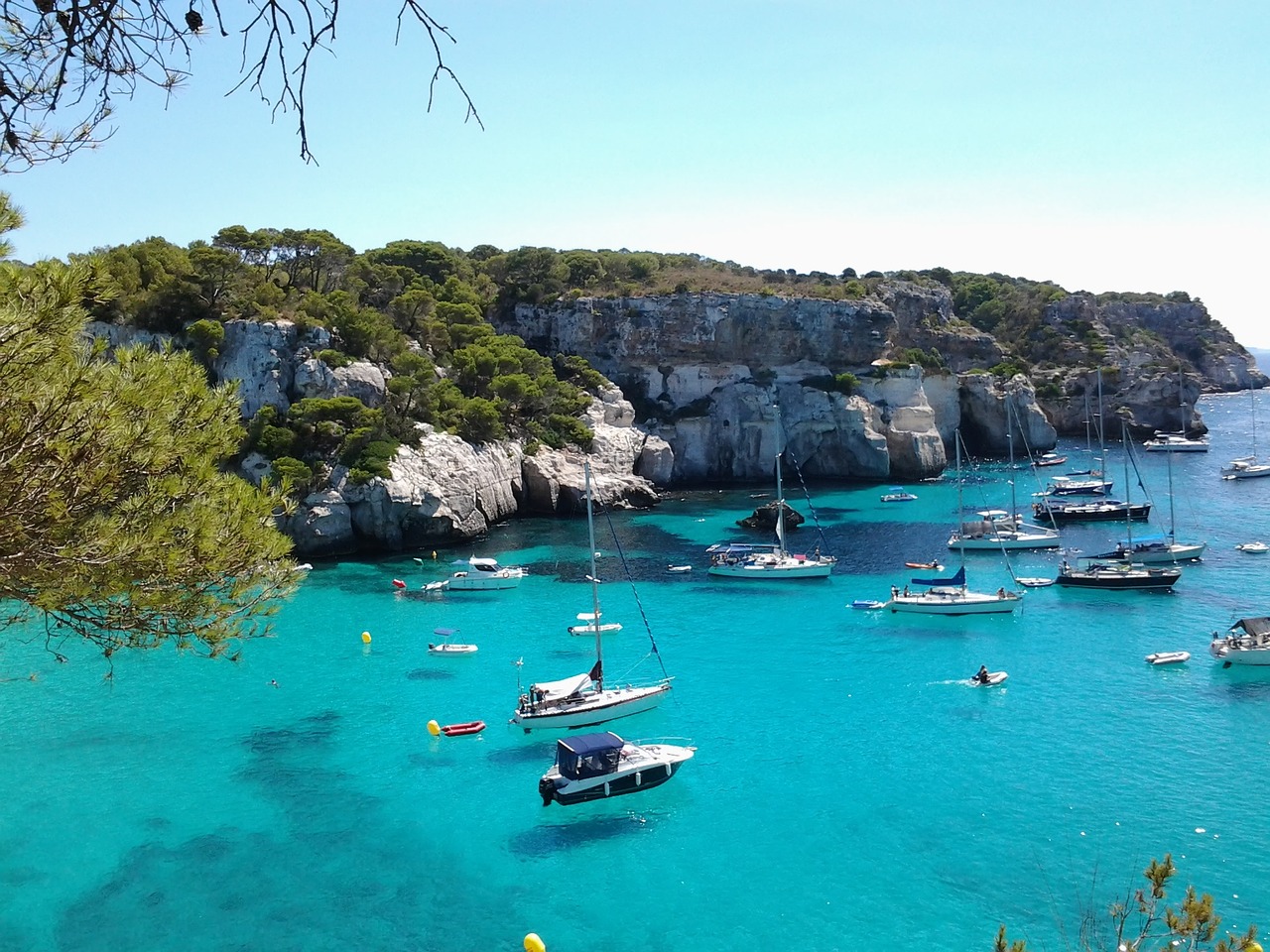 Una caletta di Minorca con acque turchesi e sabbia bianca circondata da pini mediterranei